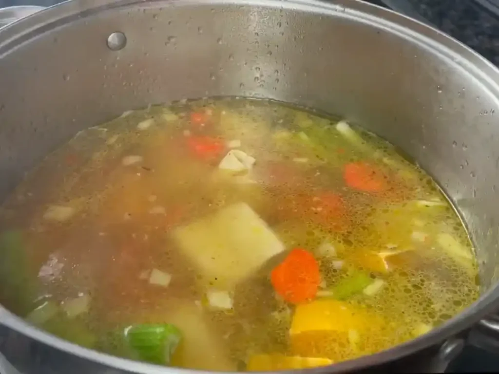 Bubbling pot of Puerto Rican Chicken Noodle Soup with vegetables.