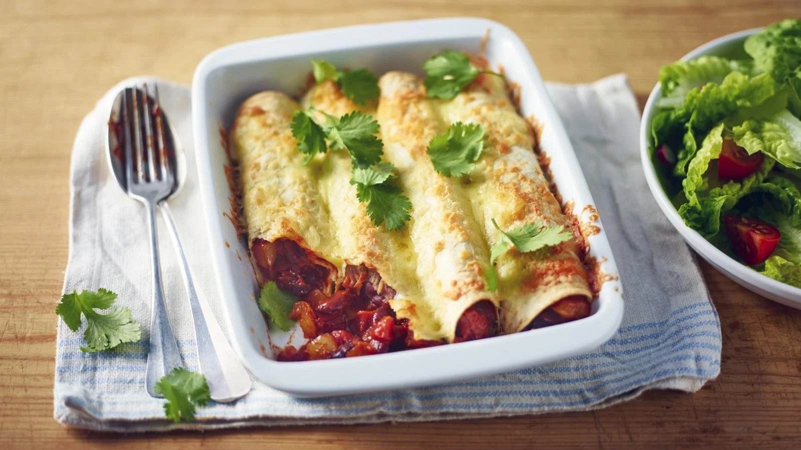 A plate of beany enchiladas garnished with fresh cilantro and avocado.