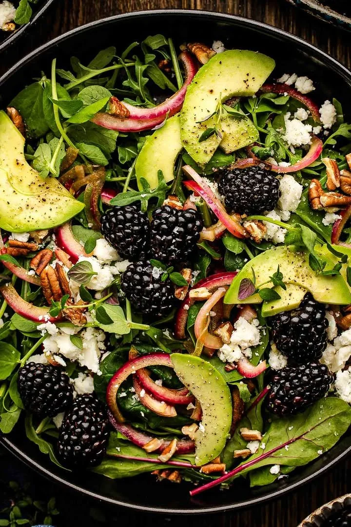 A colorful blackberry avocado salad topped with fresh herbs and a zesty dressing.