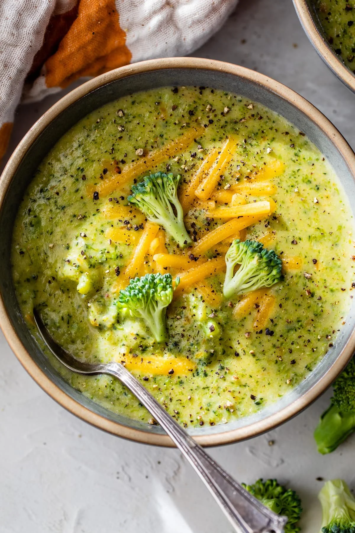 Bowl of creamy broccoli cheddar soup topped with shredded cheese.