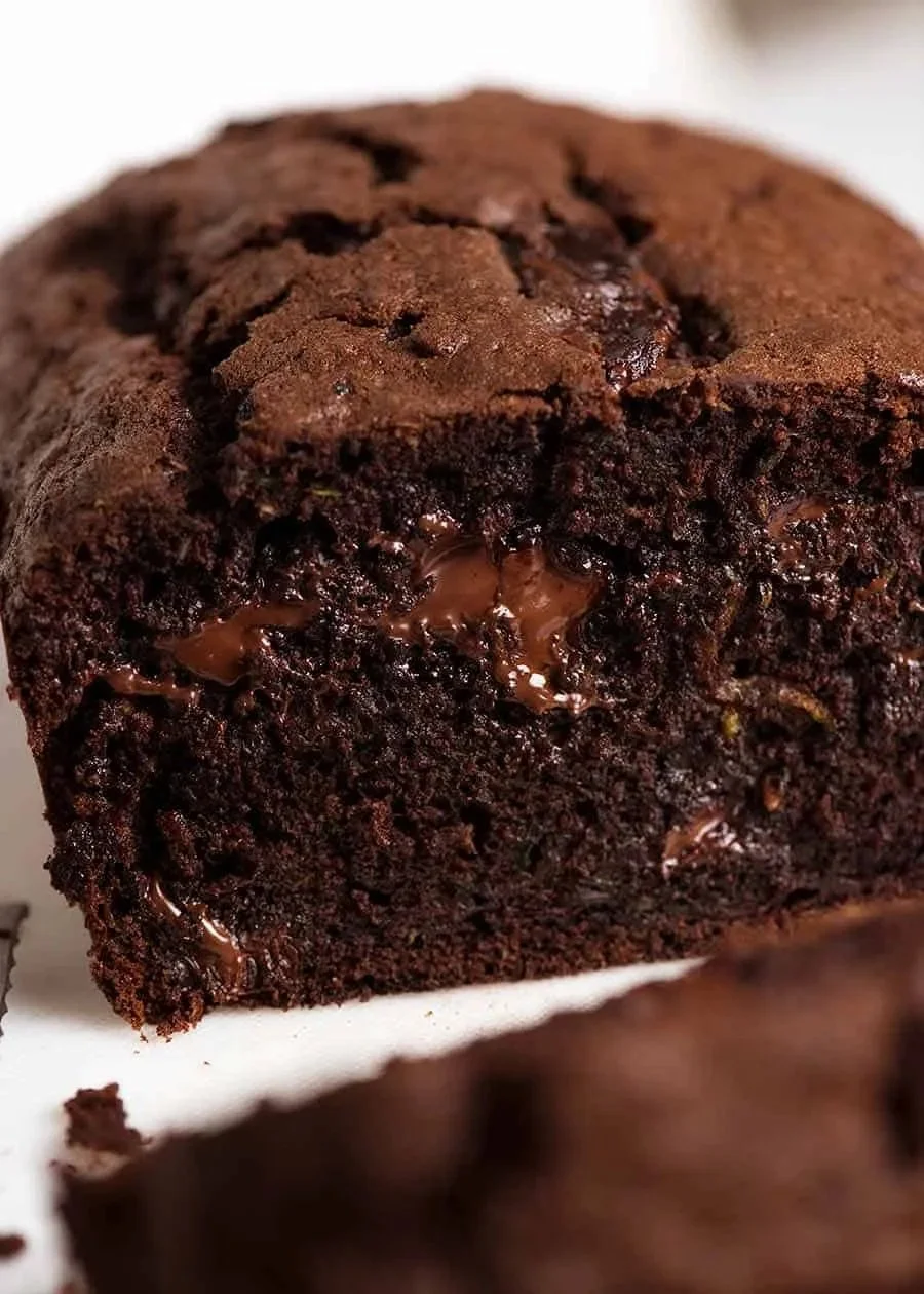 A slice of rich chocolate zucchini bread on a wooden table.