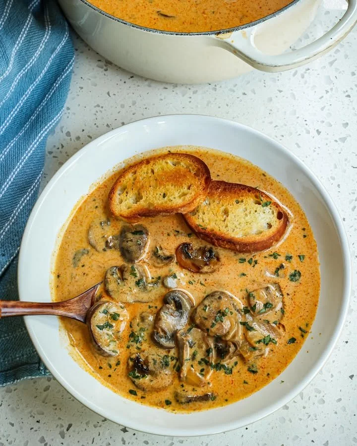 A bowl of creamy Hungarian Mushroom Soup garnished with herbs and mushrooms.