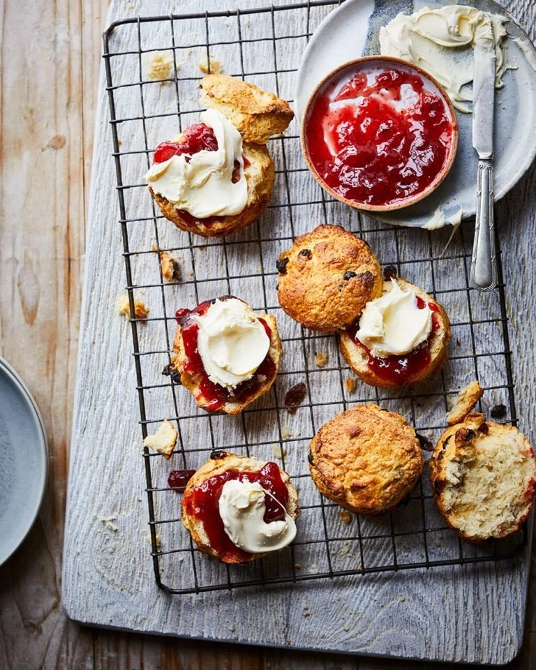 Freshly baked fruit scones on a wooden table with fruits around them.