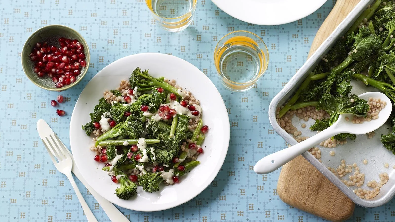 Plate of greens topped with giant couscous and tahini sauce, showcasing a healthy meal option.