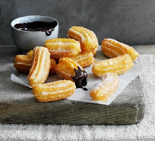 Homemade churros with hot chocolate sauce on a rustic background