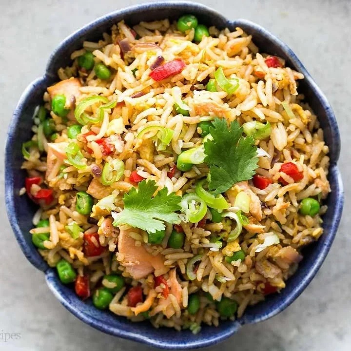 A colorful plate of salmon fried rice garnished with green onions and vegetables.