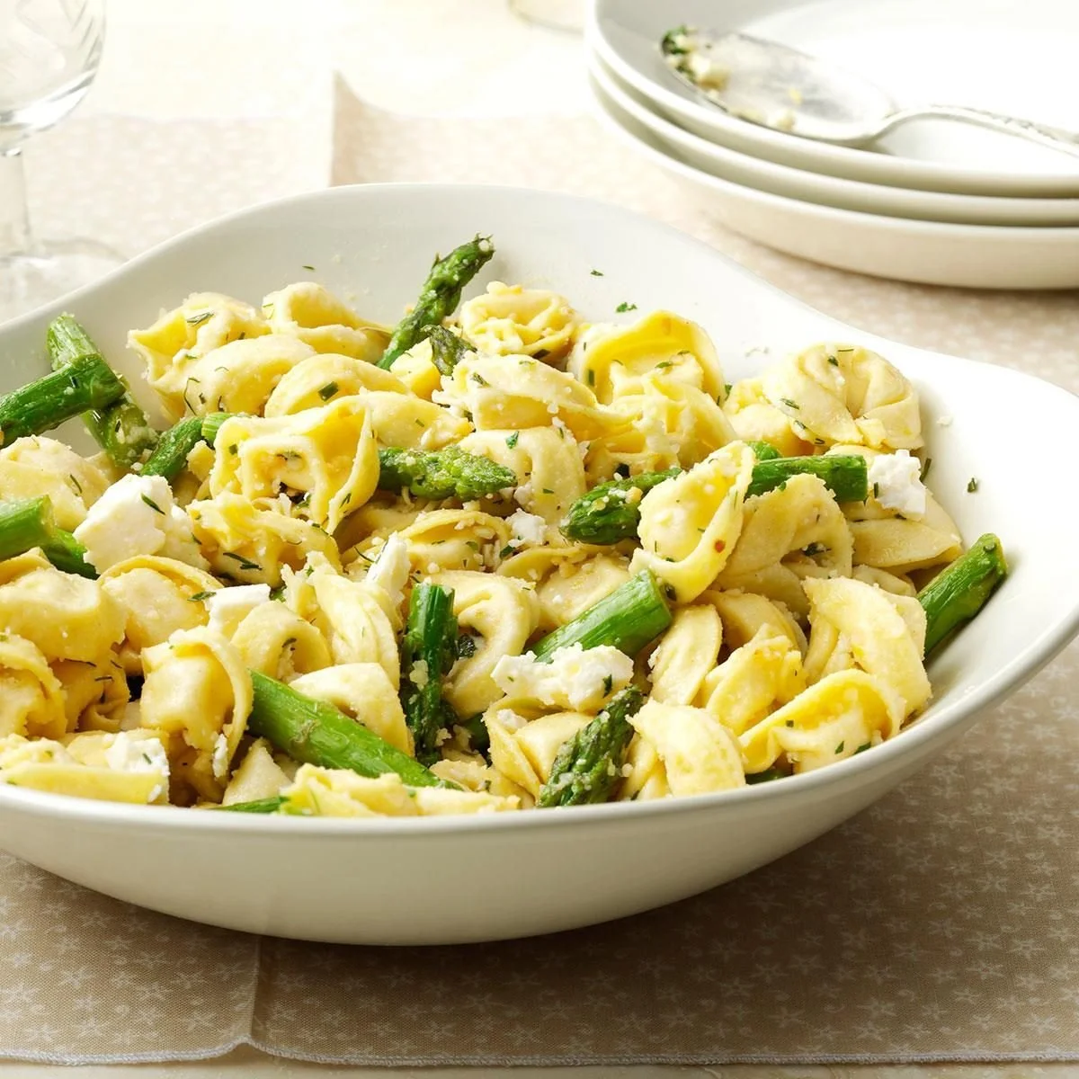 Plate of tortellini with asparagus and lemon, garnished with herbs.