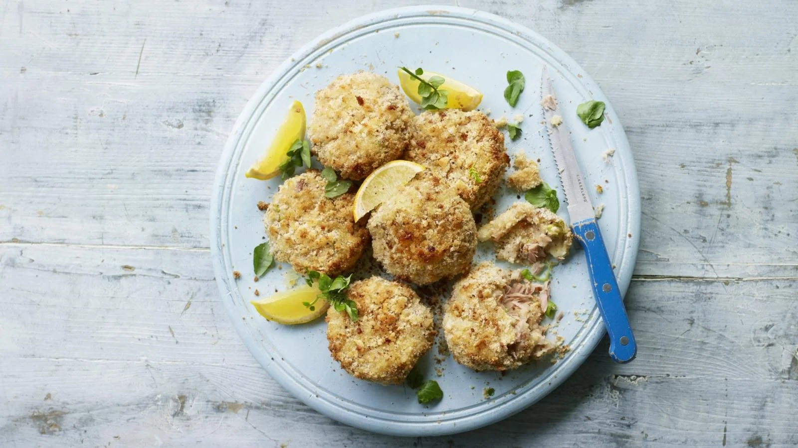 Plate of homemade tuna fishcakes with herbs and lemon on a rustic wooden table