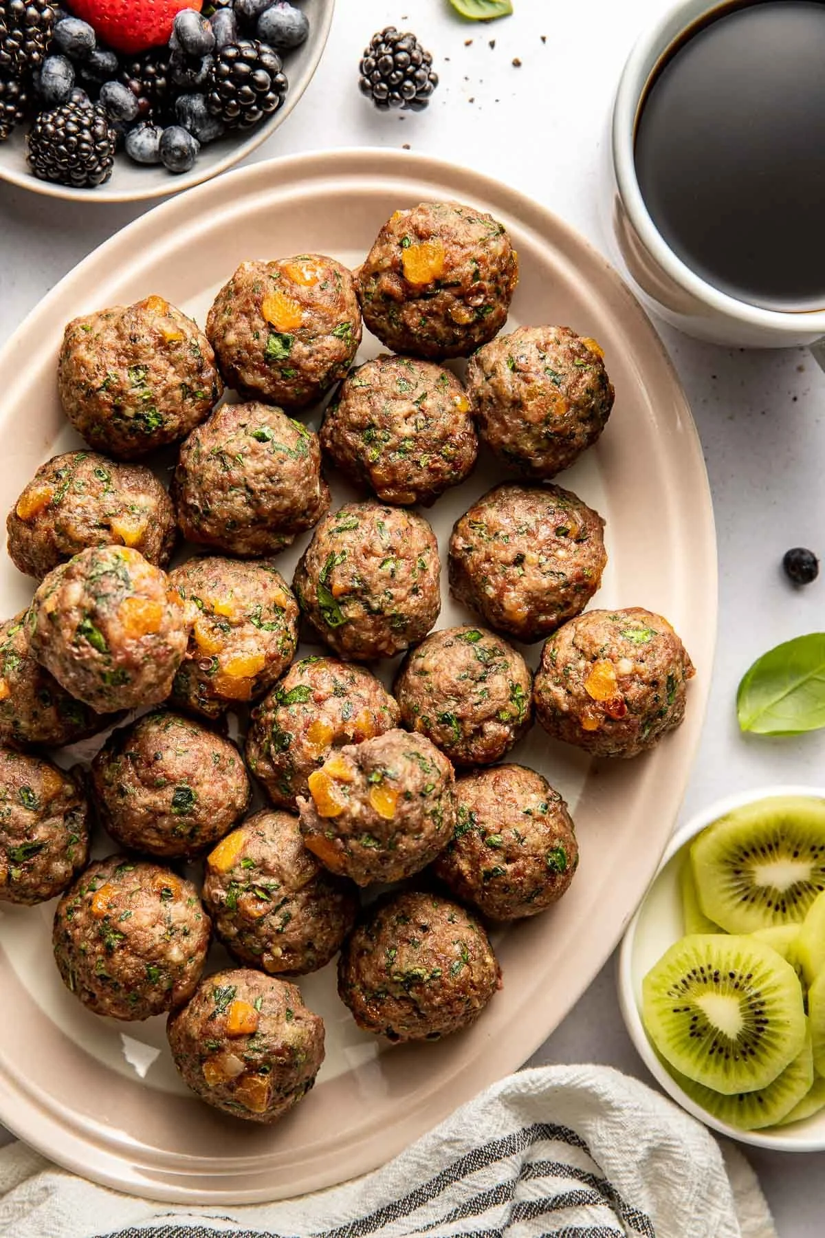 Apricot basil breakfast meatballs on a plate, garnished with fresh herbs.