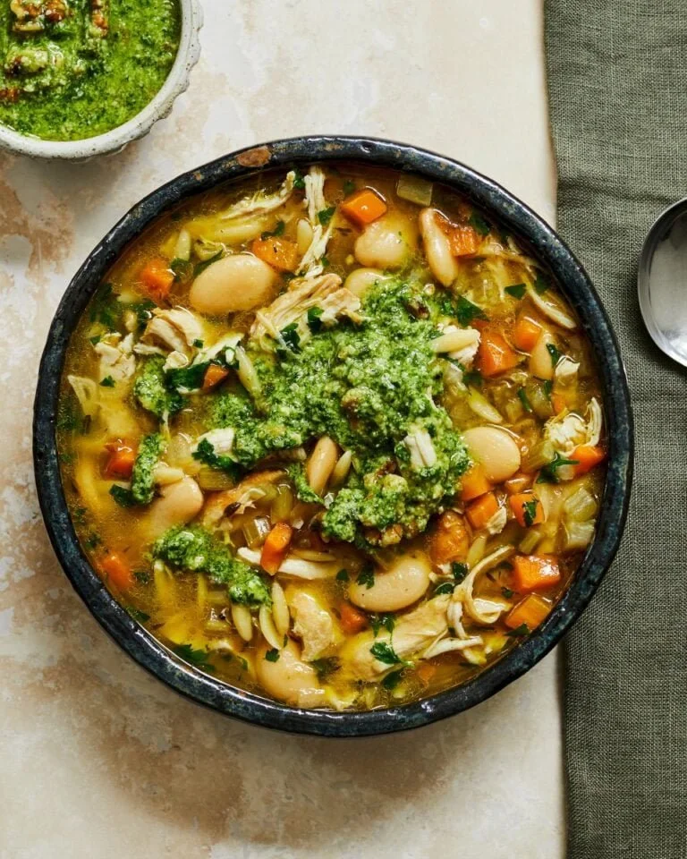 Bowl of chicken soup with beans and orzo topped with walnut pesto