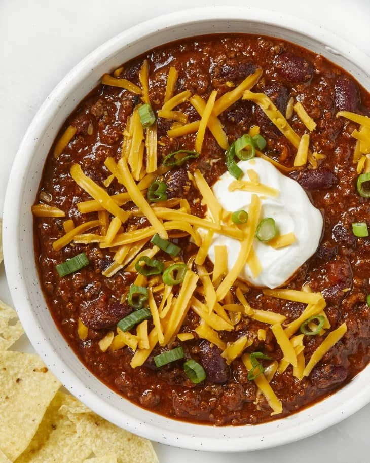 A bowl of classic beef chili topped with cheese and herbs, served with cornbread.