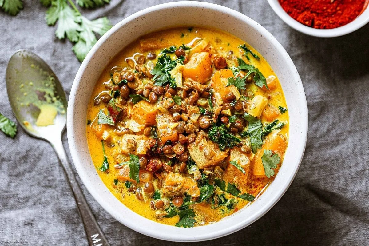Coconut butternut and lentil stew in a bowl with fresh herbs on top
