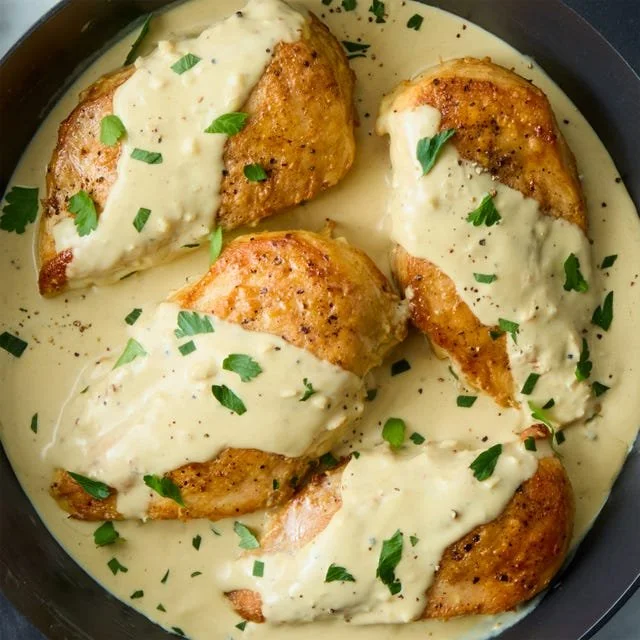 Creamy Dijon chicken in a skillet garnished with herbs and served with vegetables.