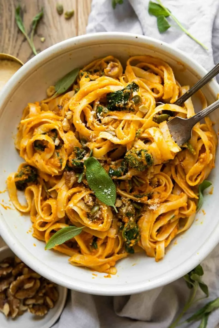 Bowl of creamy pumpkin pasta garnished with herbs and parmesan cheese