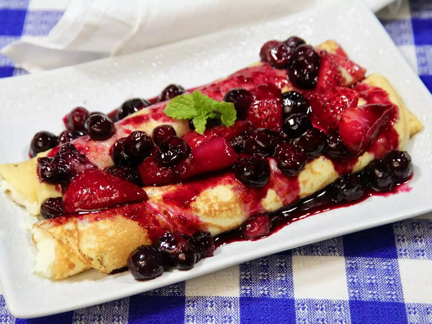 Delicious easy blender crepes on a plate with strawberries and syrup