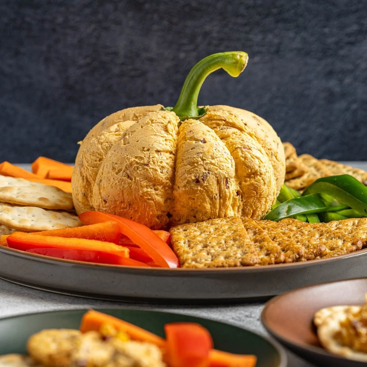 Festive Pumpkin Cheese Ball served with crackers and garnished with herbs