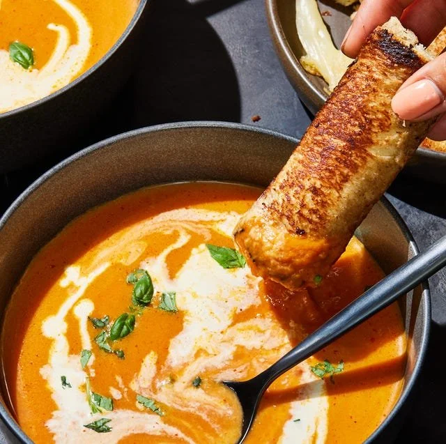 Bowl of pumpkin tomato soup with grilled Swiss cheese sticks on the side