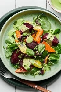 Roasted beet salad drizzled with green goddess dressing on a white plate