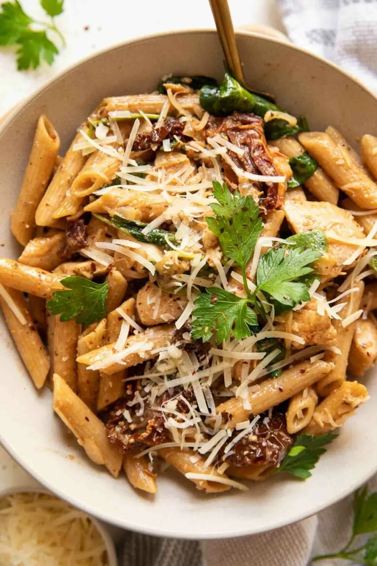 Delicious Sun Dried Tomato Chicken Pasta served with fresh herbs and Parmesan cheese