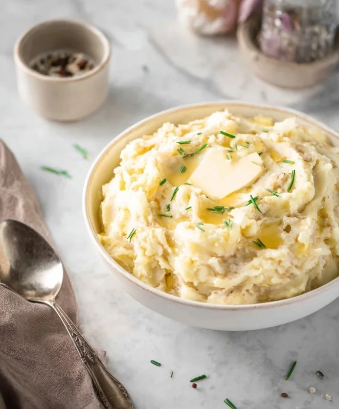 Bowl of creamy mashed potatoes topped with butter and parsley
