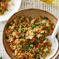 Plate of air fryer fried brown rice garnished with vegetables and herbs.